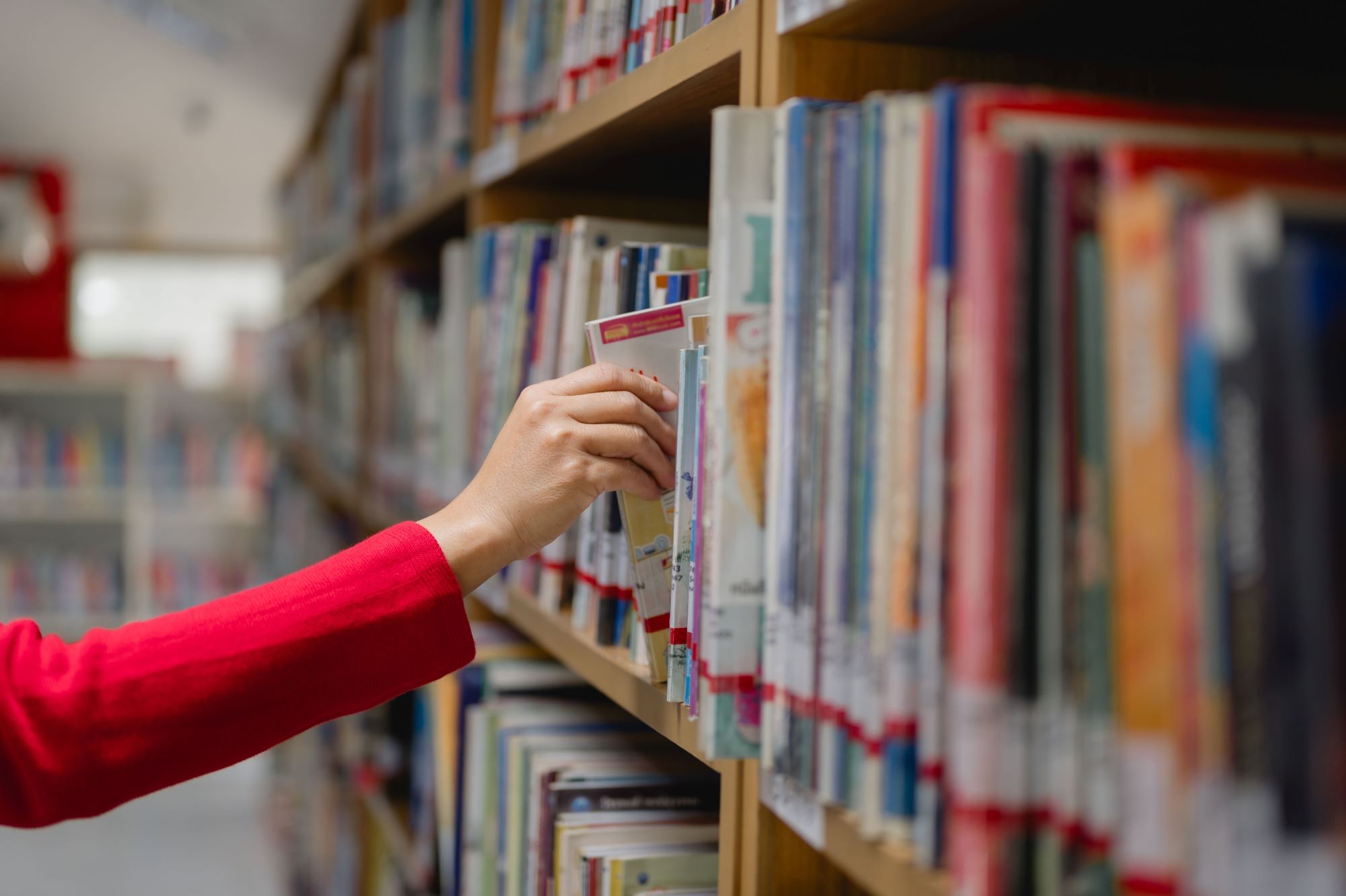 library row, hand with red sleeve reaching for a book from the shelf